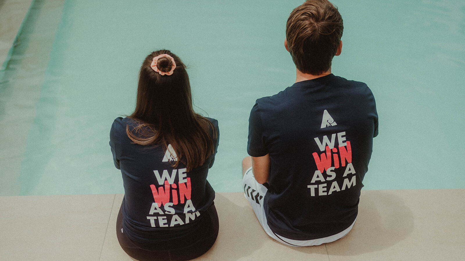 2 seated people from behind with "We win as a team" on the T-shirt © Alissa Lüpke - www.alissa.luepke.us