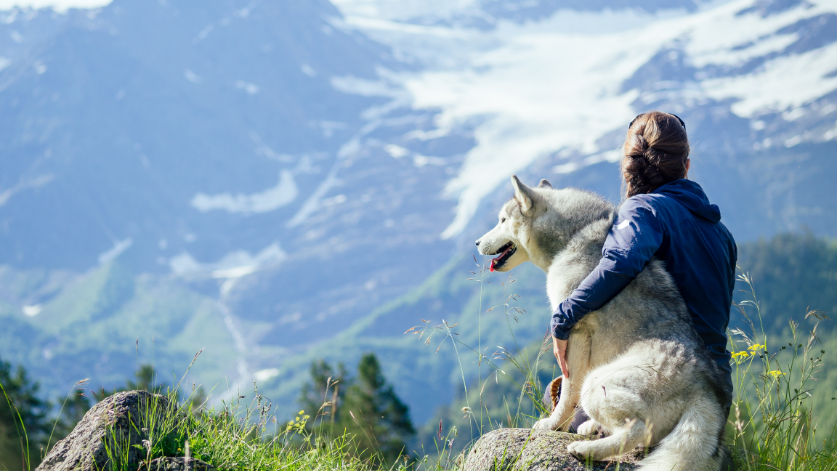 Frau umarmt Hund vor einem Bergpanorama